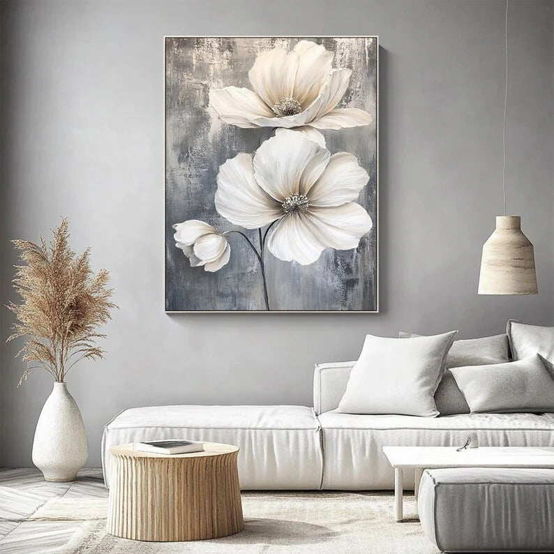 a living room with a large floral painting hanging on the wall above a white sofa. The painting depicts three large white flowers with delicate petals, creating a serene and elegant atmosphere in the room.