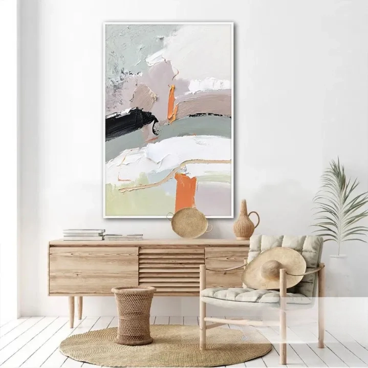 a modern and minimalist living room with a large abstract painting hanging on the wall above a wooden dresser. The dresser has a woven basket and a vase on it, adding a touch of natural elements to the space. A chair is placed in front of the dresser, and a potted plant is located next to it, creating a cozy and inviting atmosphere.