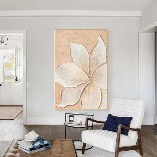 a living room with a large, detailed painting of a flower hanging on the wall. The room has a white chair, a coffee table, and a bookshelf, creating a cozy and inviting atmosphere.