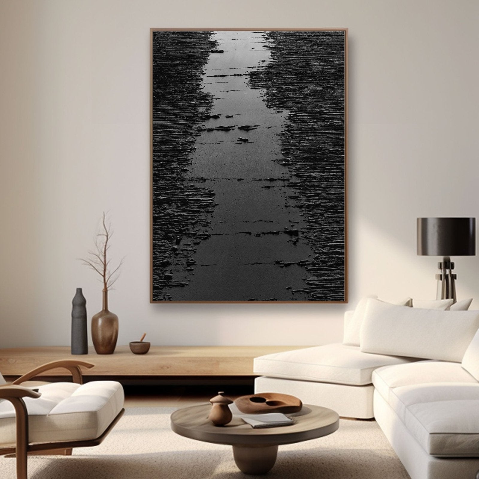 a modern living room with a large black and white abstract painting hanging on the wall. The room is furnished with a white sofa, a wooden coffee table, and a wooden side table with a vase and a bowl. The overall design and color scheme create a minimalist and sophisticated atmosphere.