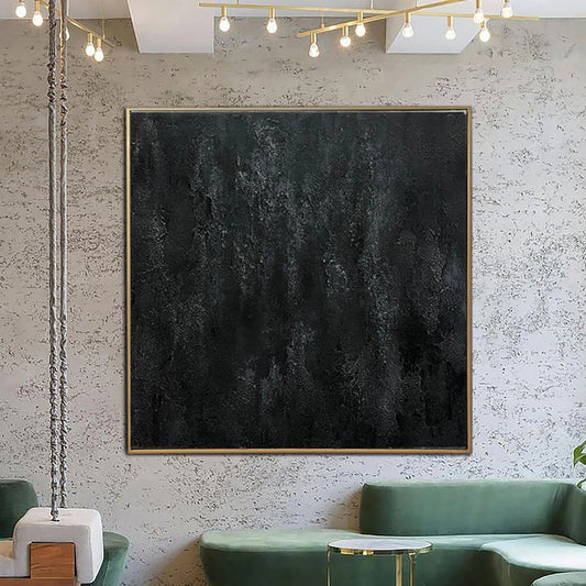 a modern living room with a large black square artwork hanging on the wall above a green couch. The room has a minimalist and contemporary design, with a white wall and a wooden floor.