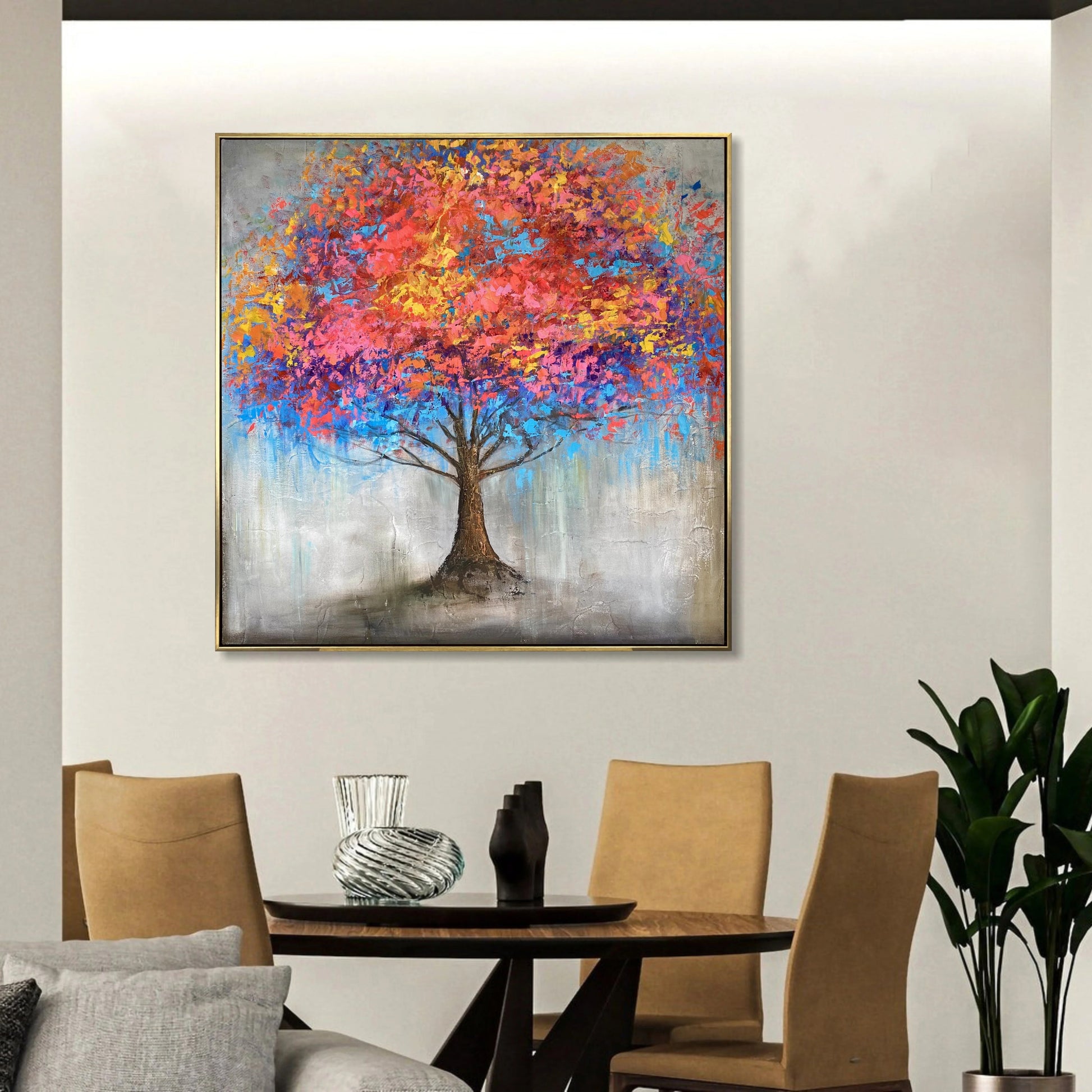 a large, colorful painting of a tree hanging on a wall above a wooden dining table with four chairs.