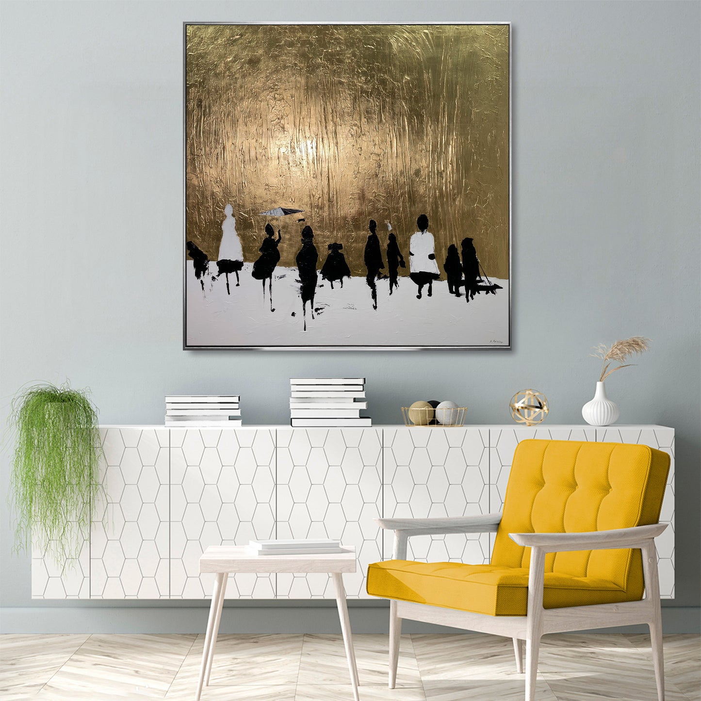 a modern living room with a large abstract painting hanging on the wall above a white cabinet with a geometric pattern. The painting depicts a group of people in a snowy landscape, with a golden background. The room also includes a yellow armchair, a white side table, and a potted plant, creating a cozy and stylish atmosphere.