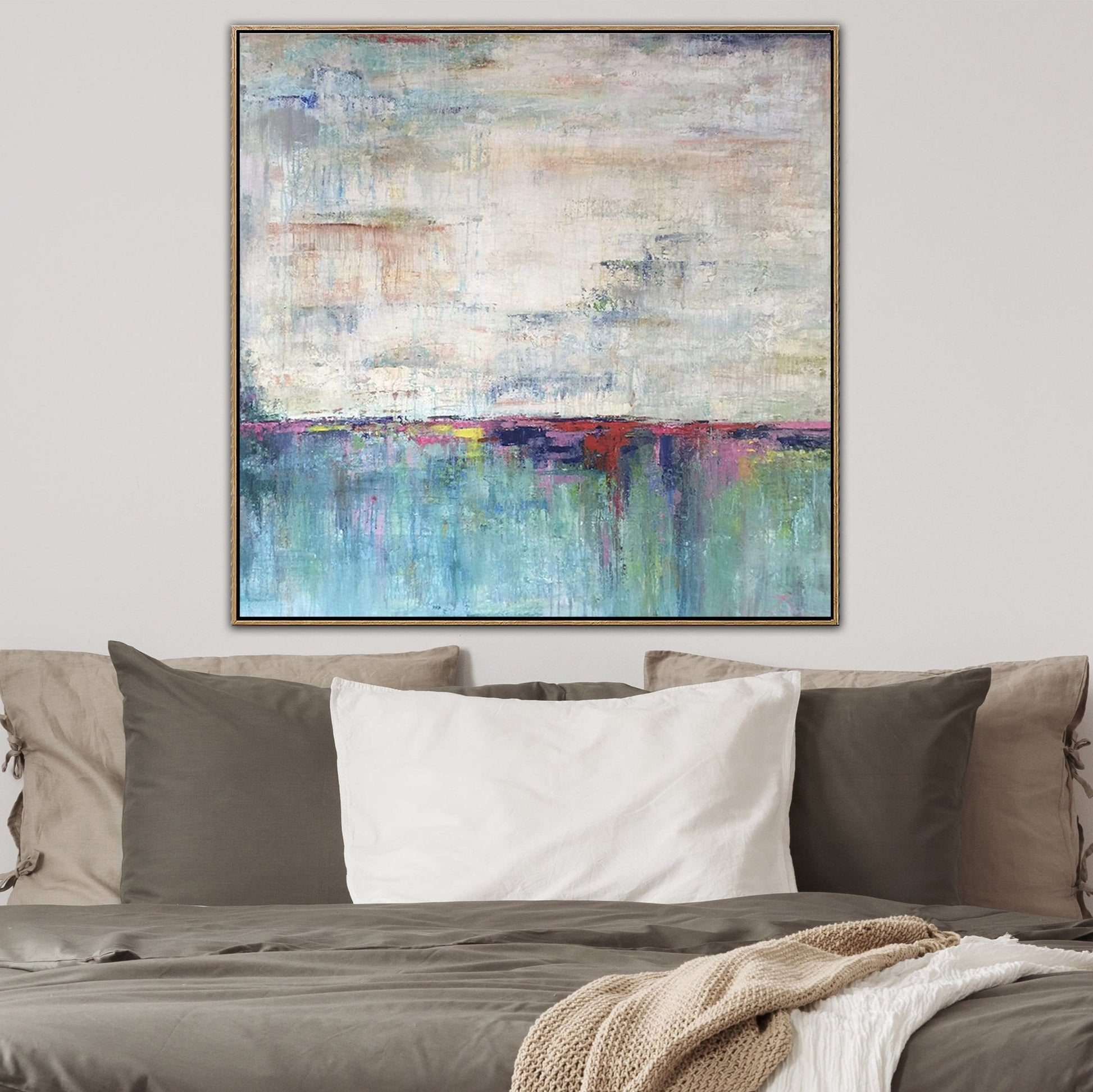 a large abstract painting hanging on a wall above a bed with pillows.
