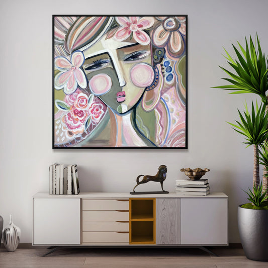 a large, colorful abstract painting of a woman's face hanging on a wall above a white cabinet with drawers. The cabinet has a decorative metal horse figurine on top. The room also includes a potted plant and some books, creating a cozy and artistic atmosphere.