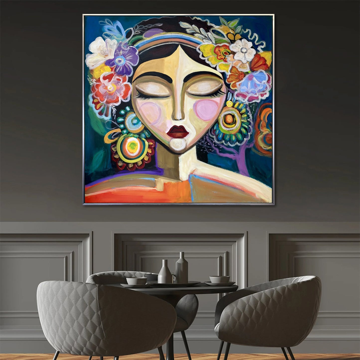 a large, colorful painting of a woman's face with a flower crown on her head, hanging on a wall above a dining table with chairs.