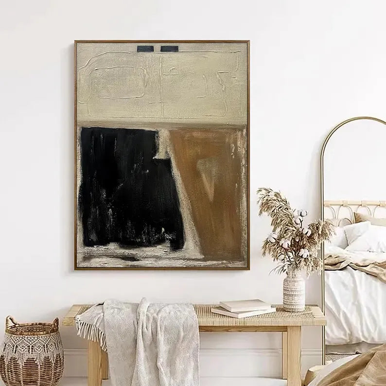 a large abstract painting hanging on a white wall above a wooden bench. The painting has a black and white color scheme, with a large black shape and a smaller brown shape. The bench is positioned in front of the painting, and there is a vase of dried flowers on the bench.