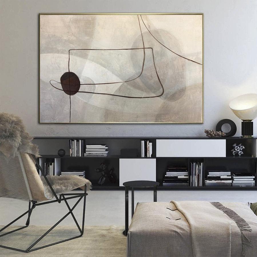 a modern living room with a large abstract painting hanging on the wall above a black bookshelf filled with books. The room also includes a black chair, a gray ottoman, and a black side table.