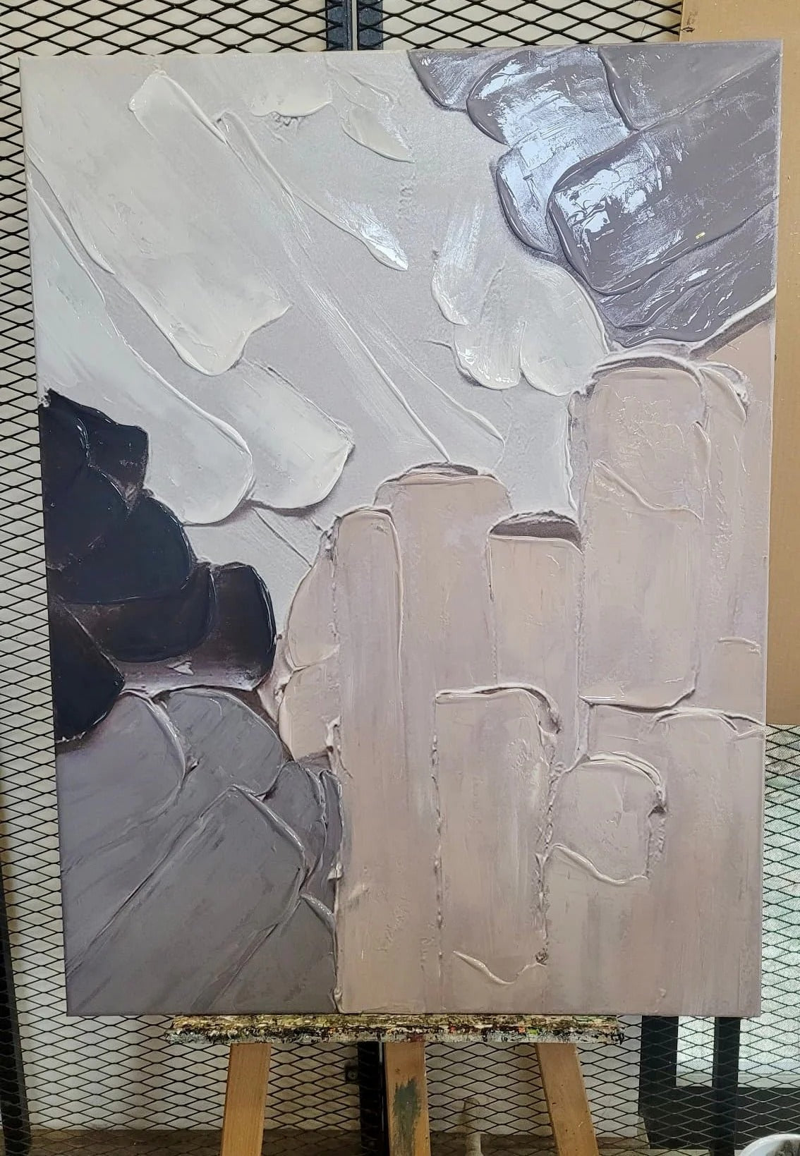 The image is an abstract painting displayed on an easel, featuring a mix of light and dark colors.