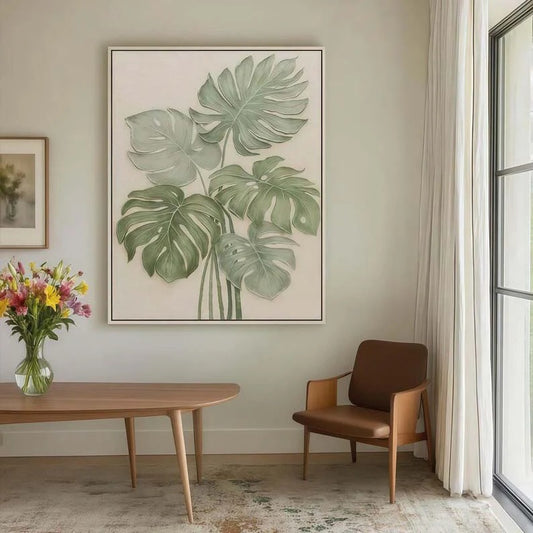a living room with a large framed painting of green monstera leaves hanging on the wall, a wooden table with a vase of colorful flowers, and a brown armchair.