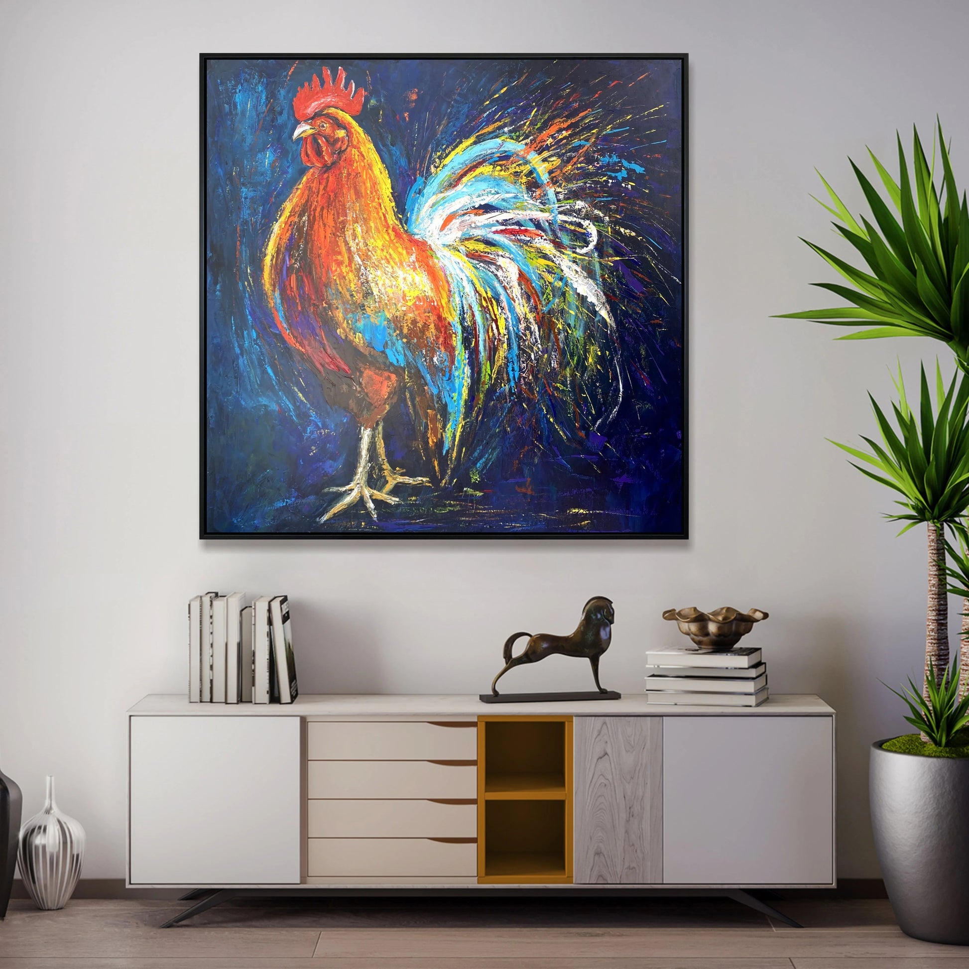 a vibrant painting of a rooster, which is hanging on a wall above a white cabinet with drawers. The painting is surrounded by various decorative items, including a potted plant, a sculpture, and a stack of books.