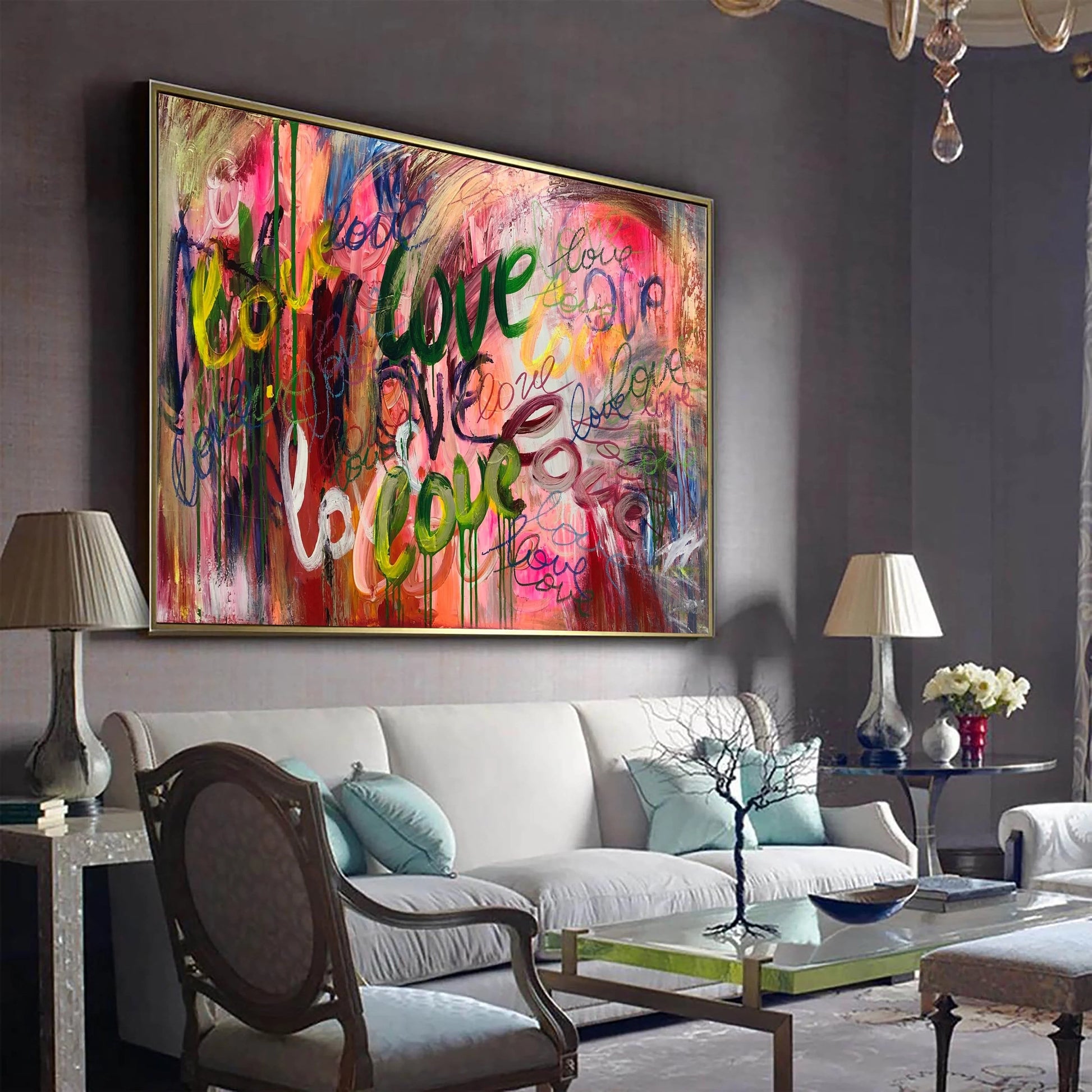 a large, colorful abstract painting hanging on a wall in a living room. The painting has a mix of pink, green, blue, and yellow colors, creating a vibrant and lively atmosphere. The living room is furnished with a white sofa, a wooden chair, and a glass coffee table. There are also two lamps and a vase on the table, adding to the cozy and inviting ambiance of the space.