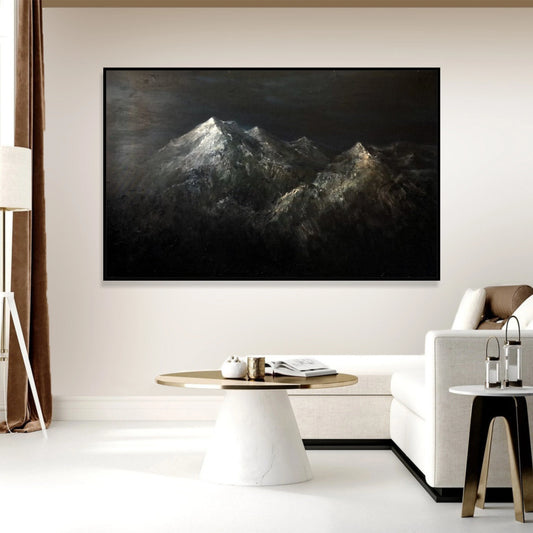 a large, dark-toned painting of a mountain range hanging on a white wall above a white coffee table in a modern living room setting.