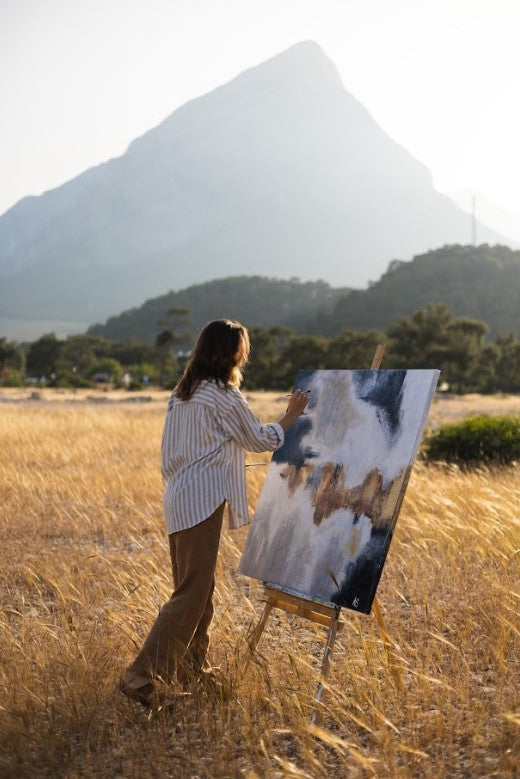 a woman standing in a field painting a picture